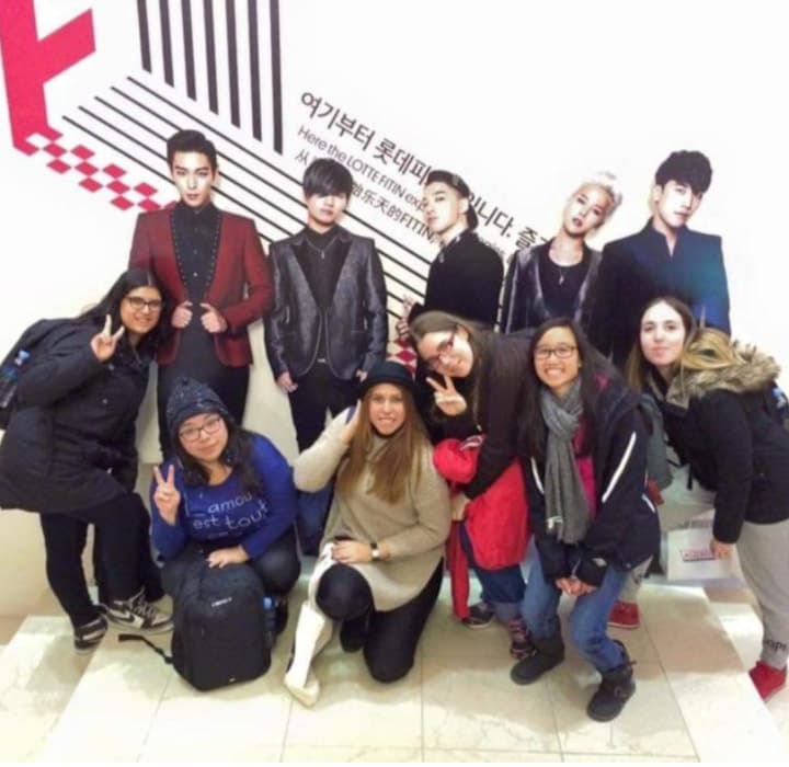 Grupo de pasajeras junto a poster de banda de kpop 